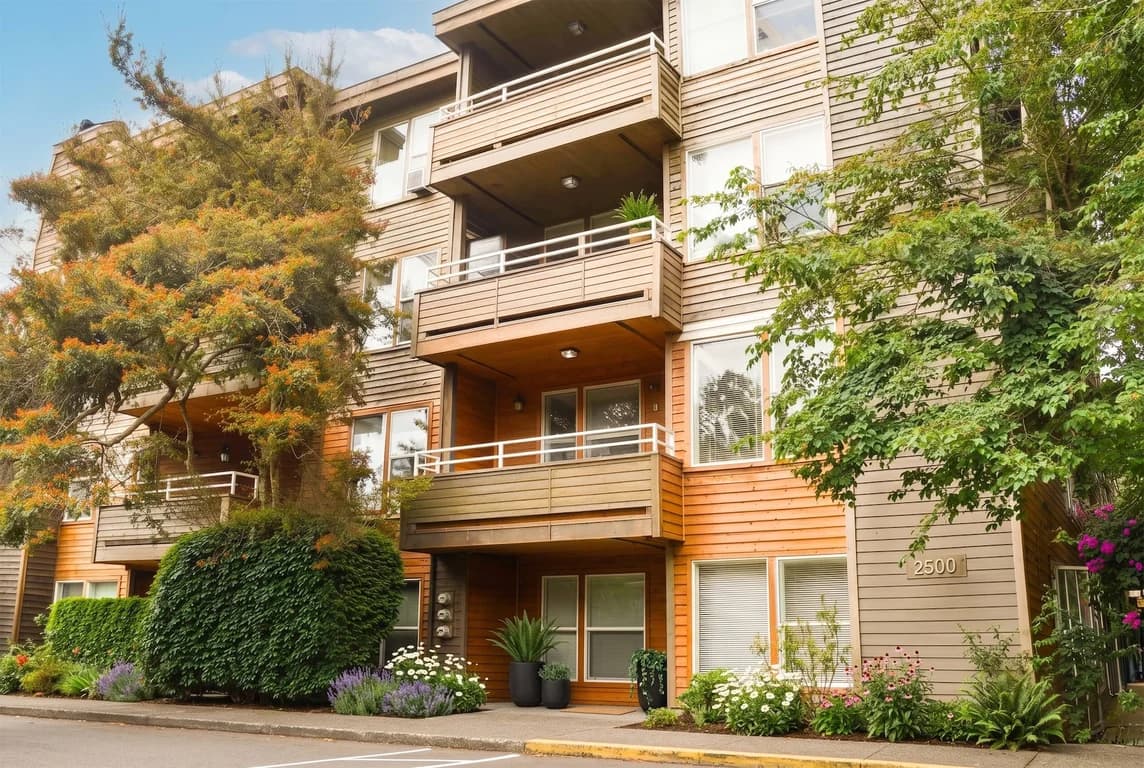 Exterior view of Westwood Court apartment building with wood siding, multiple balconies, and lush...