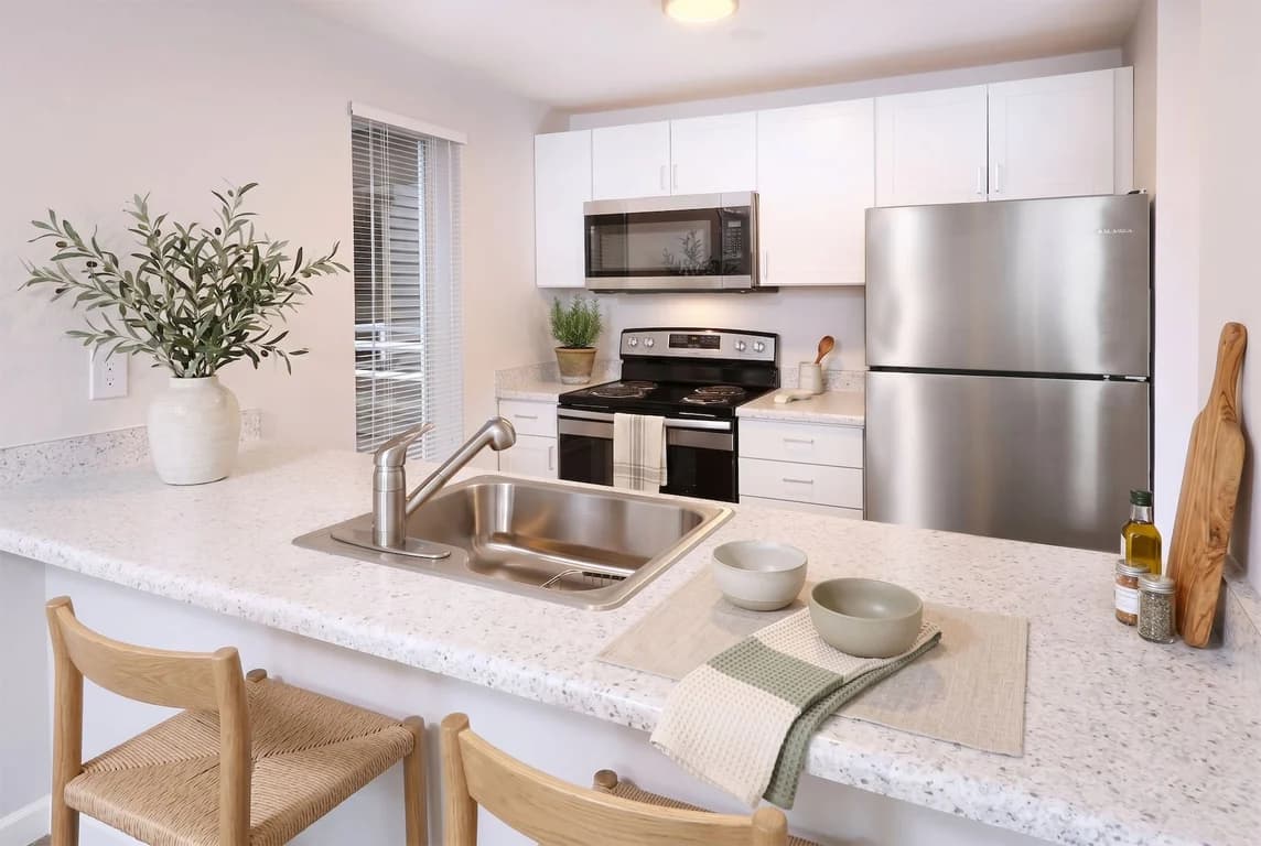Kitchen with white cabinets, speckled countertops, stainless steel appliances, and a bar seating ...
